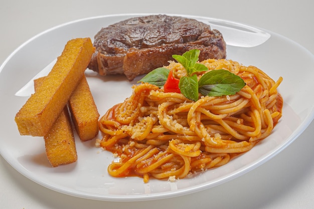 Foto espaguete ao molho sugo com parmesão servido com filé e polenta frita