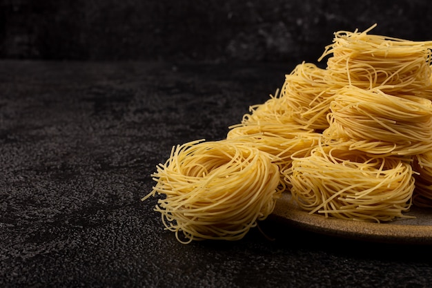 Espaguete Capellini em um prato de cerâmica em um fundo escuro estrutural com espaço para copiar. Espaguete