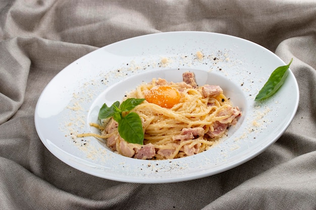 Espaguete Carbonara na chapa branca sobre fundo têxtil