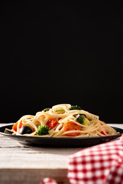 Espaguete com legumes brócolis tomate pimentão na mesa de madeira