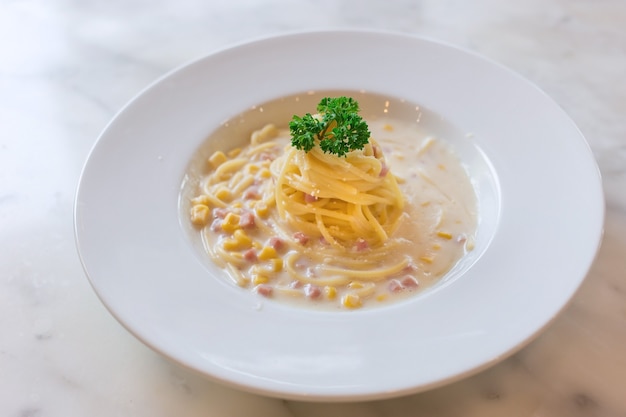 Espaguete com molho de creme de presunto e milho colocado em um prato branco na mesa de mármore como pano de fundo.