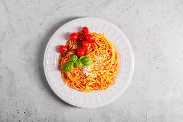 Espaguete com molho de tomate e tomate cereja com manjericão em uma mesa de concreto branca