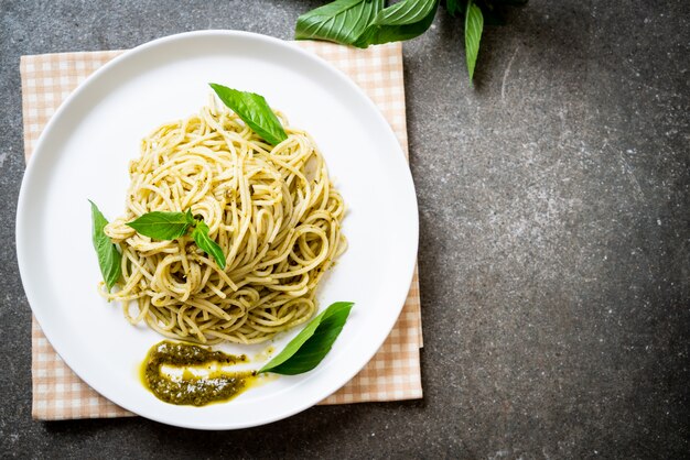 Espaguete com molho pesto, azeite e folhas de manjericão.