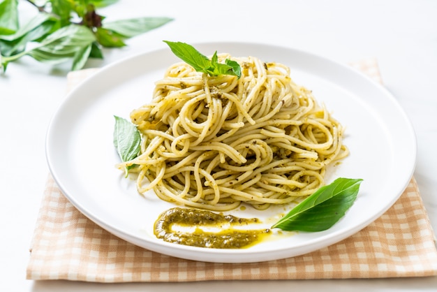 Espaguete com molho pesto, azeite e folhas de manjericão.