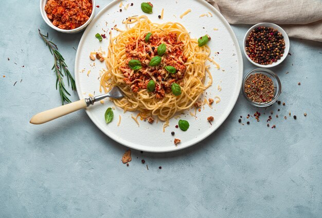 Espaguete e molho de tomate grosso com manjericão e queijo em um fundo cinza-azulado.