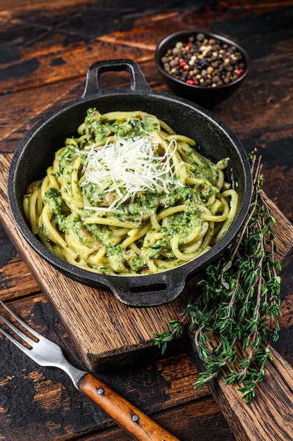 Espaguete macarrão com molho pesto, espinafre e parmesão em uma panela. fundo de madeira escuro. vista do topo.