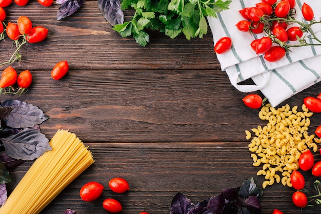 espaguete, manjericão e tomate em um fundo de madeira