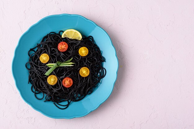 Espaguete preto de vista superior com tinta de choco com tomate cereja amarelo e vermelho em placa azul em fundo rosa com espaço de cópia, conceito de hora de comer