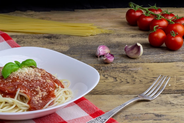 Espaguete vegetariano em uma mesa de madeira, tomate, alho e macarrão no fundo