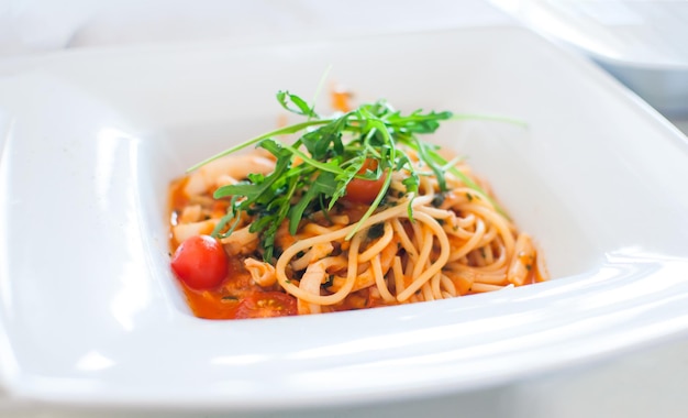 Espagueti con calamar y vista de ángulo de rúcula de tomate y limón en plato cuadrado blanco