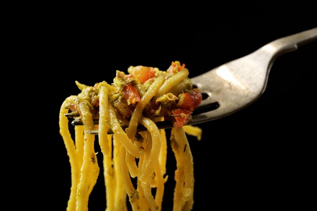 Espagueti de pasta italiano en tenedor sobre fondo negro