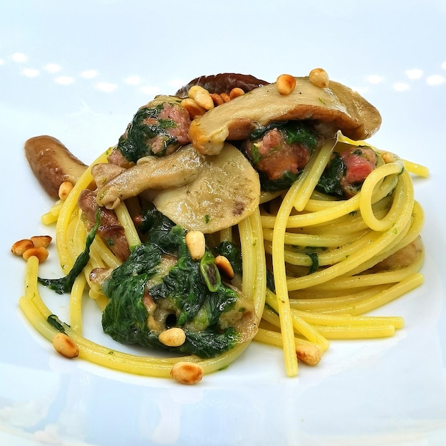 Foto espagueti con salchichas, espinacas, hongos y piñones