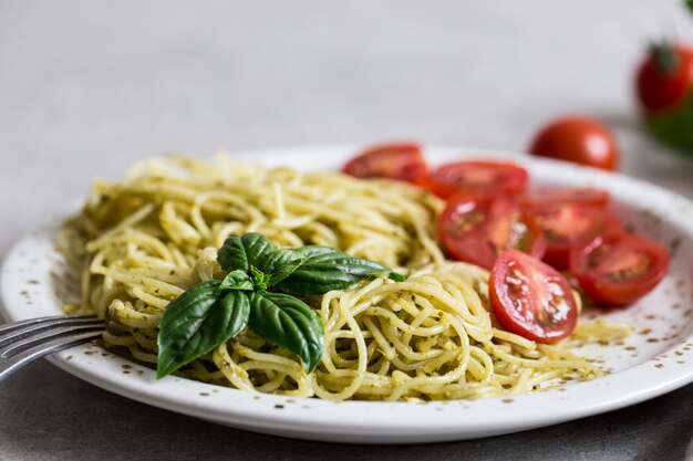 Espagueti con salsa de pesto casero, hojas de albahaca y tomates