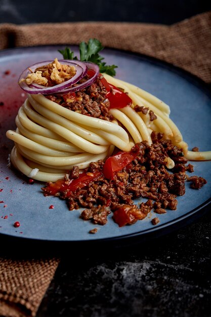 Espaguetis a la boloñesa Concepto Cocina italiana Espaguetis bellamente dispuestos en un plato y regados con salsa de carne boloñesa Placa azul fondo oscuro