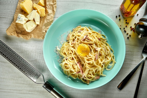 Espaguetis carbonara de pasta italiana con salsa bechemal, tocino y yema de huevo, queso parmesano, servido en un plato azul sobre una mesa de madera. Comida de restaurante.