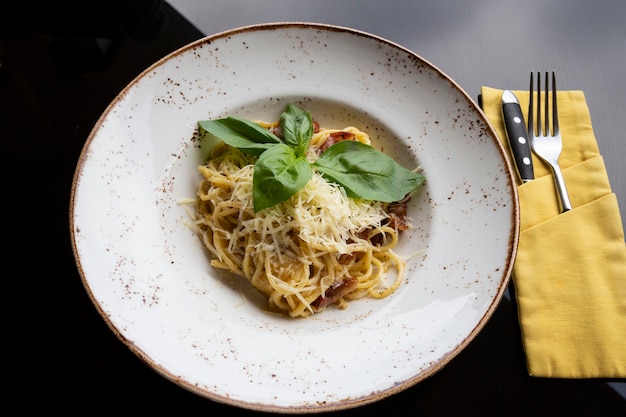 Espaguetis a la carbonara en un plato blanco sobre la mesa de un restaurante. Pasta de trigo duro con bacon, queso y salsa de nata. De cerca