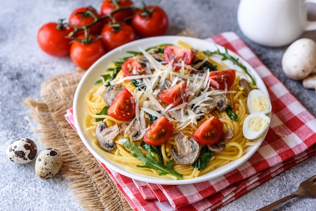Espaguetis con champiñones, queso, espinacas, rukkola y tomates cherry. Plato italiano, cultura mediterránea