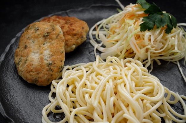 Espaguetis con chuleta y ensalada en un plato negro