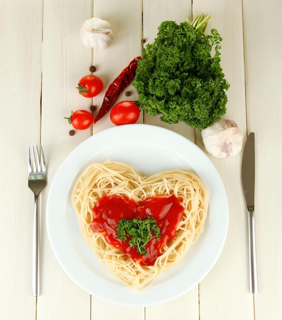 Espaguetis cocidos cuidadosamente dispuestos en forma de corazón y cubiertos con salsa de tomate, sobre fondo de madera