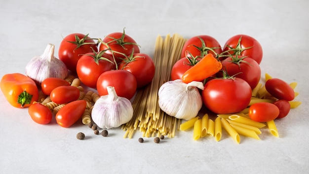 Espaguetis crudos Penne Fusili Tomatoess Dientes de ajo Pimienta naranja sobre fondo gris
