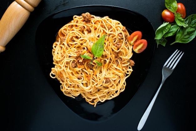 Espaguetis frescos con albahaca y tomate cherry servidos en un plato aislado en la vista superior de fondo oscuro de la comida italiana
