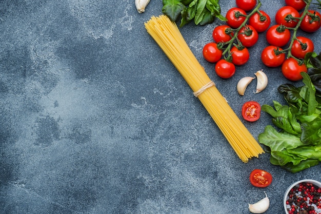 Espaguetis italianos crudos de las pastas y verdes de cocinar de los tomates de cereza de los ingredientes.