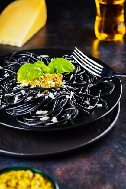 Espaguetis negros con salsa pesto, albahaca y queso parmesano. Pasta negra con tinta de sepia sobre una placa negra. Cocina tradicional italiana