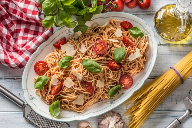 Espaguetis de pasta italiana a la boloñesa en un tazón blanco con tomates, queso parmesano y albahaca.