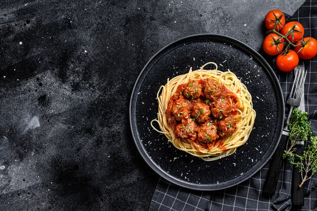 Espaguetis de pasta italiana con salsa de tomate y albóndigas. Fondo negro. Vista superior. Copia espacio