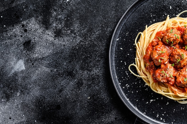 Espaguetis de pasta italiana con salsa de tomate y albóndigas. Fondo negro. Vista superior. Copie el espacio.