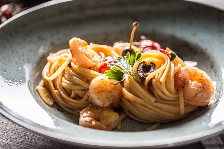 Espaguetis de pasta en plato y sartén con salsa de tomate y camarones toatoes y hierbas. Cocina italiana o mediterránea.