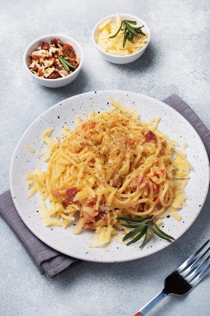 Espaguetis de pasta con queso de huevo de tocino en un plato con especias. Plato tradicional italiano Carbonara. Mesa de hormigón gris