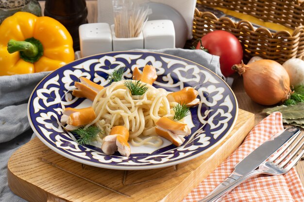 Espaguetis de pasta con salchichas hervidas y eneldo en un plato con un tradicional uzbeko