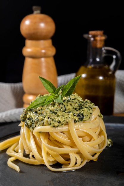 Espaguetis de pasta con salsa pesto y hojas de albahaca fresca en plato de piedra negra sobre fondo de madera.