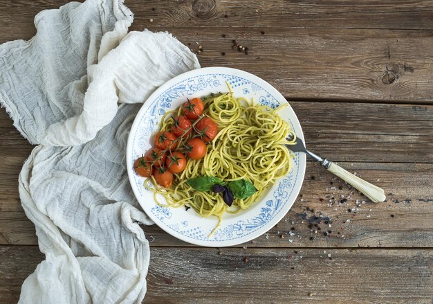 Espaguetis de pasta con salsa de pesto tomates cherry al horno con albahaca en tabke de madera rústica vista superior de la mesa oscura