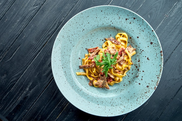 Espaguetis de pasta tradicional con salsa de crema, ternera y tomate, rúcula, servidos en un plato azul sobre una superficie de madera negra. cocina italiana