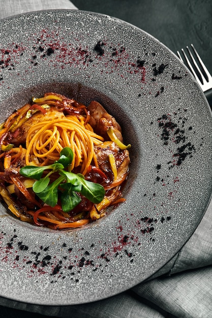 Espaguetis con pato y verduras. Cocina italiana, hermosa porción de pasta en un plato gris y espacio oscuro.