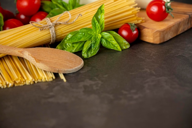 Espaguetis sobre fondo oscuro, queso, tomate y albahaca