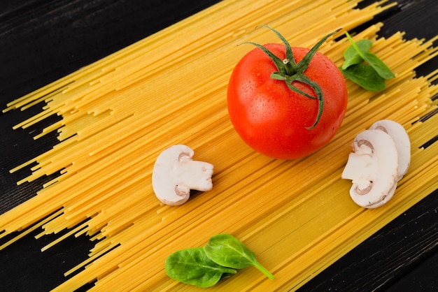 Espaguetis con tomate, champiñones y espinacas sobre fondo negro. Vista superior. Concepto de alimentación saludable Preparación de productos.