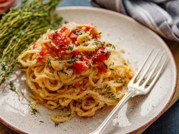 Espaguetis con tomate y tomillo en un plato sobre una mesa azul