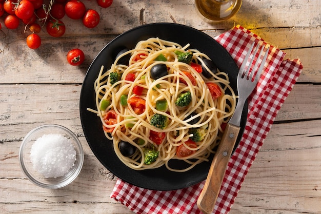 Espaguetis con verduras brócolito tomate pimientos sobre mesa de madera