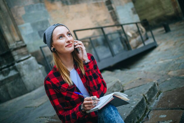 españa, barcelona, retrato, de, mujer joven, sonriente, en el teléfono, sentado, en, escaleras, con, cuaderno