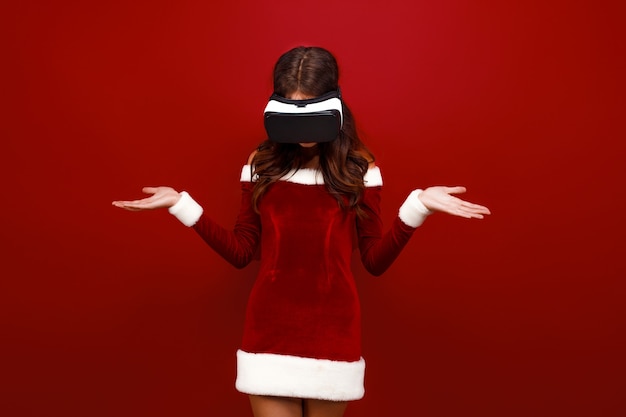 Espantada com a jovem santa no vestido de Natal, olhando no fone de ouvido, apontando as mãos de lado isoladas no vermelho w.