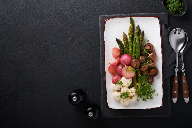 Espargos cogumelos mozzarella queijo rabanete grelhado e salada de agrião azeite salada na placa cerâmica retangular no fundo da mesa de concreto preto Dieta saudável conceito de comida grelhada Vista superior