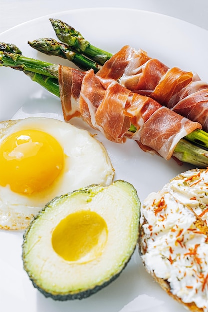 Espargos fritos envoltos em bruschetta de ovos fritos de jamon com queijo macio e abacate em um prato branco