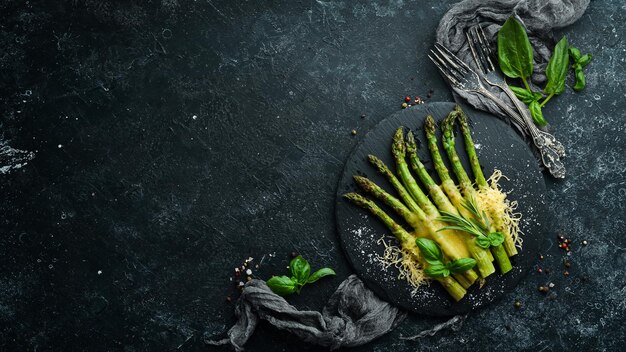 Espárragos al horno con queso y albahaca en un plato de piedra negra Vista superior Espacio libre para el texto