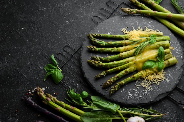 Espárragos al horno con queso y albahaca en un plato de piedra negra Vista superior Espacio libre para el texto