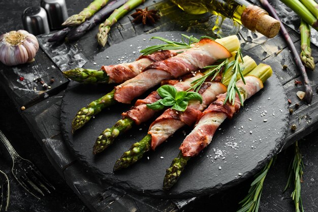 Espárragos al horno con tocino y especias en un plato de piedra negra Vista superior Espacio libre para el texto