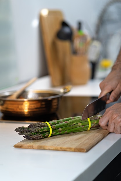 Espárragos frescos en la cocina con la mano del hombre, chef cortando espárragos.