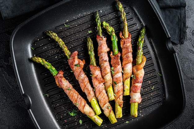 Espárragos fritos envueltos en tocino en una sartén a la parrilla Fondo negro Vista superior